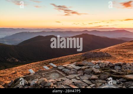 Am frühen Morgen auf dem Gipfel des Berges. Blick von der Bergspitze auf das bergige Gelände. Sonnenaufgang hoch in den Bergen. Stockfoto