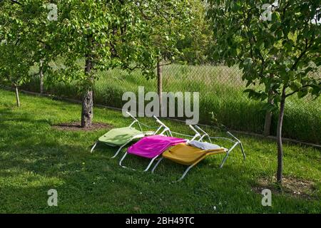 Drei Leinenliegenstühle im schönen Hof warten darauf, dass die Sonne zu ihnen durchbricht. Stockfoto