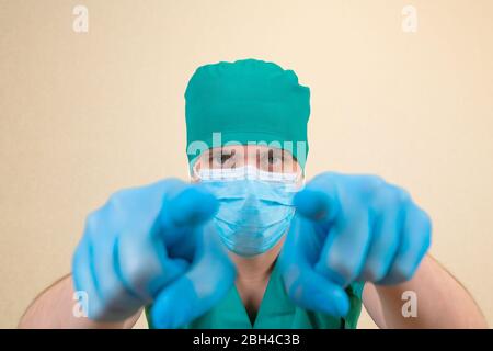Arzt trägt grünen Schutzanzug blaue Handschuhe und blaue Gesichtsmaske zeigen geradeaus. Stockfoto