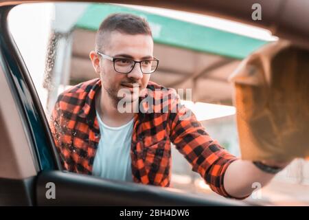 Aufnahme eines jungen Mannes, der die Fenster seines Autos von außen putzt. Stockfoto