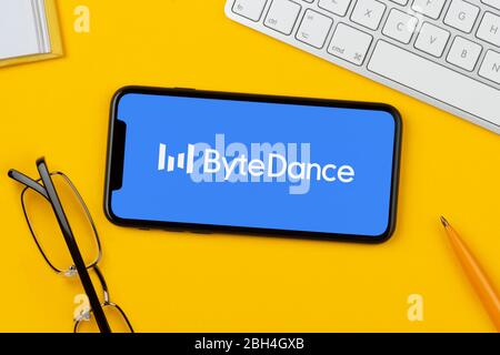 Ein Smartphone mit dem Bytedance-Logo liegt auf einem gelben Hintergrund zusammen mit Tastatur, Brille, Stift und Buch (nur für redaktionelle Verwendung). Stockfoto