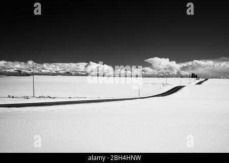 Eine leere Straße durchschneidet eine schneebedeckte Winterlandschaft, in Schwarz und Weiß dargestellt. Tetonia, Idaho Stockfoto