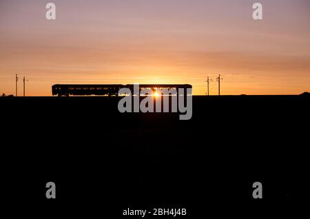 Northern Rail Klasse 156 Super Sprinter Diesel 2 Wagenzug auf der elektrifizierten Westküste Hauptlinie macht einen Sonnenuntergang Silhouette Stockfoto