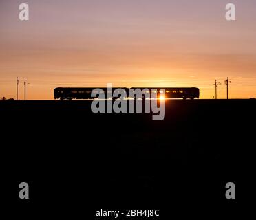 Northern Rail Klasse 156 Super Sprinter Diesel 2 Wagenzug auf der elektrifizierten Westküste Hauptlinie macht einen Sonnenuntergang Silhouette Stockfoto