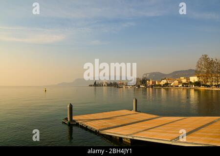 Panoramasicht auf den Gardasee von einem hölzernen Pier mit der Altstadt von Bardolino im Hintergrund bei Sonnenuntergang, Provinz Verona, Venetien, Italien Stockfoto