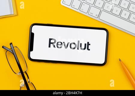 Ein Smartphone mit dem Revolut-Logo liegt auf einem gelben Hintergrund zusammen mit Tastatur, Brille, Stift und Buch (nur für redaktionelle Verwendung). Stockfoto