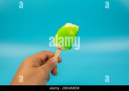 Mann Hand hält Eis Popsicle Limette Geschmack auf blauem Hintergrund. Stockfoto