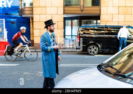 London, Großbritannien - 22. Juni 2018: Portier Portier in traditioneller Kleidung Hut und blauen Mantel stehen am Hoteleingang mit dem Auto hilft mit Gepäck Stockfoto