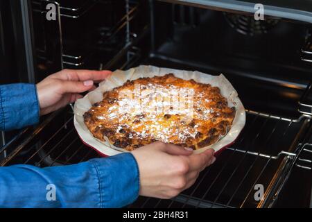 Gebackener Quark-Auflauf. Mädchen legt einen Käsekuchen in den Ofen. In roter Backform. Stockfoto