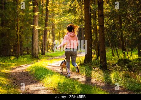 Junge Frau und Hund laufen zusammen auf dem Land im Wald. Fröhliche Frau Ausübung im Freien mit ihrem Haustier. Stockfoto