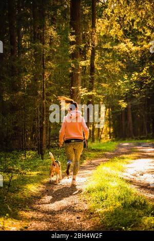 Junge Frau und Hund laufen zusammen auf dem Land im Wald. Fröhliche Frau Ausübung im Freien mit ihrem Haustier. Stockfoto