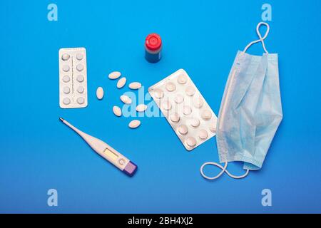 Medikamente, Pillen, ein Thermometer und eine medizinische Maske auf blauem Hintergrund.Covid 19 Stockfoto