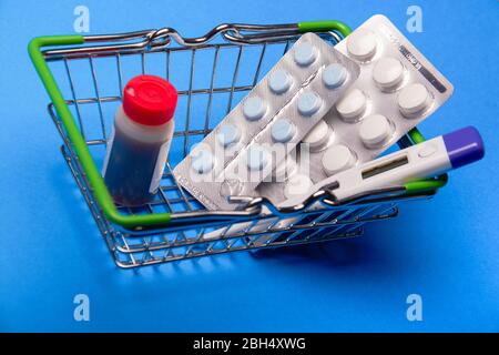 Korb mit Medikamenten, Tabletten und einem Thermometer auf blauem Hintergrund Stockfoto