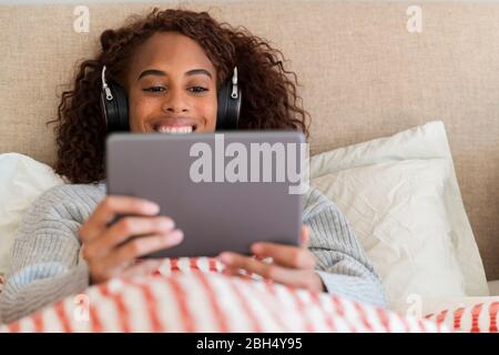 Lächelnde Frau mit Tablet und Kopfhörer im Bett Stockfoto