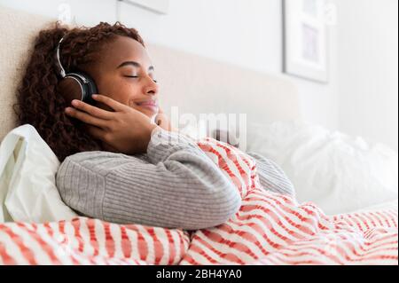 Lächelnde Frau mit Kopfhörern im Bett Stockfoto