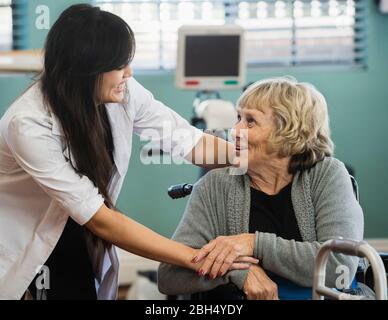 Lächelnder Arzt und ältere Frau, die die Hände im Rehabilitationszentrum hält Stockfoto
