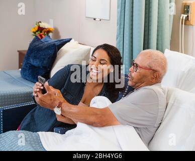 Lächelnde Frau und lächelnder älterer Mann, der auf das Smartphone schaut Stockfoto