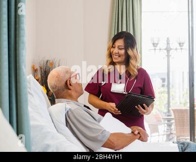 Lächelnde Krankenschwester hält Zwischenablage von älteren Mann im Bett Stockfoto