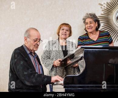 Ältere Frauen singen mit einem älteren Mann, der Klavier spielt Stockfoto
