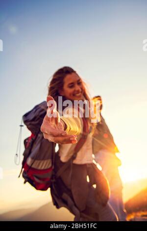 Menschen helfen sich gegenseitig, bei Sonnenaufgang einen Berg hinauf zu wandern. Stockfoto