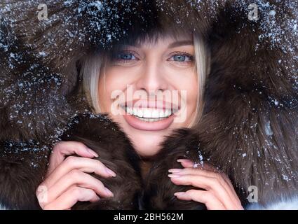 Glückliche Frau in Pelzhaube Blick auf Kamera. Nahaufnahme des Hochformatfotos. Frostigen Winter Porträt. Stockfoto