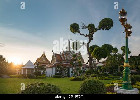 Die atemberaubende Aussicht bei Sonnenuntergang vom Wat Arun Ratchawararam Ratchawaramahawihan, während die Sonne den Tempel erhellt. Grüne Bonsai Bäume und Garten. Stockfoto