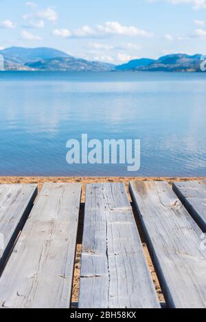 Verwitterter grauer Picknicktisch im Vordergrund mit Blick auf See und Berge im Hintergrund Stockfoto