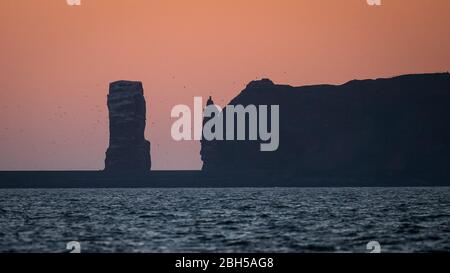 23. April 2020, Schleswig-Holstein, Helgoland: Hinter den Klippen von Helgoland geht die Sonne auf. Startschuss für ein großes maritimes Testfeld vor Helgoland: Wissenschaftler des Testzentrums für Maritime Technologien haben in Tonnen eine Fläche von drei Millionen Quadratmetern unweit der Nordseeinsel markiert. Es soll künftig Testeinrichtungen für die maritime Robotik bereitstellen. Hersteller und Wissenschaftler können dort verschiedene Szenarien testen. So können beispielsweise autonome Unterwasserfahrzeuge für Offshore-Windenergieanlagen unter realen Bedingungen im Meer oder im Drohnenflug getestet werden Stockfoto