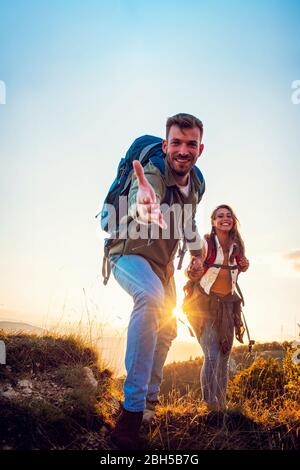 Menschen helfen sich gegenseitig, bei Sonnenaufgang einen Berg hinauf zu wandern. Stockfoto