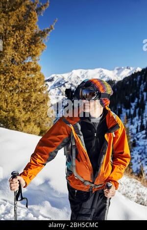 Portrait von Skifahrer in orange Jacke und Maske bei Snow Mountain Hintergrund an einem sonnigen Tag Stockfoto