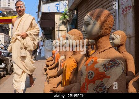 Ein Jain Priester in Mumbai, Indien, geht neu gemachte Tonfiguren der hinduistischen Göttin Durga, die für Durga Puja (Festival) gemacht wurde, und setzte in die Sonne zum Trocknen Stockfoto