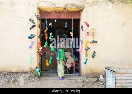 Ein kleiner Junge am Eingang eines Schuhladens. Helle farbige Kunststoff-Sandalen, Gelees, sind beliebt. In Äthiopien, Afrika. Stockfoto