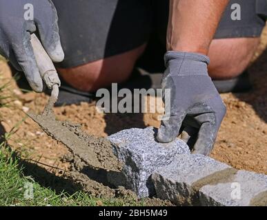 Nahaufnahme von Arbeiter mit Kelle und Handschuhe, Legen einer Rasenkante massiven Granit Blöcke als Teil der Gartenbegrenzung Stockfoto