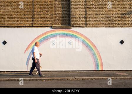 Camberwell, London, Großbritannien. April 2020. Ein Mann geht am frühen Morgen mit seinem Hund an einem Wandbild eines Regenbogens vorbei. Seit der Pandemie Covid-19 ist der Regenbogen zu einem Symbol der Unterstützung für das NHS-Personal und alle Pflegekräfte in Großbritannien geworden. Dieser Regenbogen wird von Louis Young gemalt, um dem NHS-Personal zu danken, das sich um seinen Vater kümmerte und vor kurzem aus dem Krankenhaus kam. Kredit: Tom Leighton/Alamy Live News Stockfoto