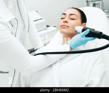 Kosmetikerin mit einer akustischen Wellenmaschine verjüngt die Haut des Gesichts einer Frau. Schmerzlose Hautverjüngung Stockfoto