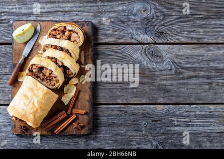 Knusprig gebackenes österreichisches Dessert: apfelstrudel aus Phylloteig mit karamellisierten Äpfeln, Nüssen, Zimt, Rosinen auf einem Holzbrett mit St serviert Stockfoto