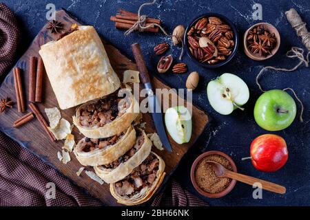 Traditioneller österreichischer Apfelstrudel aus Phylloteig mit in Scheiben geschnittenen karamellisierten Äpfeln mit braunem Zucker, Pekannüssen, Zimt, Rosinen auf schneidebo serviert Stockfoto