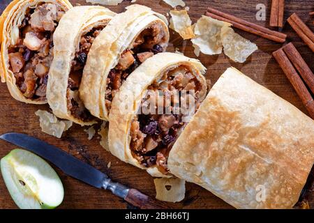 Eigelloser veganer Apfelstrudel aus Phylloteig mit in Scheiben geschnittenen karamellisierten Äpfeln mit braunem Zucker, Pekannüssen, Zimt, Rosinen auf Holzschnitt serviert Stockfoto