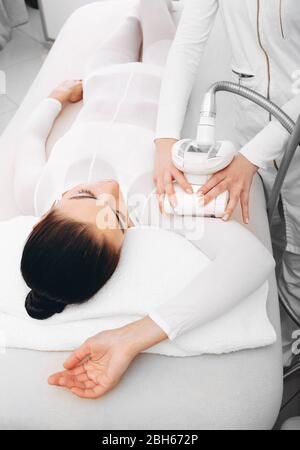 Frau, die während der LPG-Massage bequem auf einem Massagetafel liegt. Kosmetikerin entfernt Kululitis auf der Hand einer Frau Stockfoto