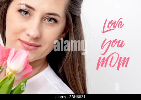 Love You Mama rosa Text und junge Frau mit rosa Tulpen auf weißem Hintergrund. Junge Mutter mit Blumen. Stockfoto