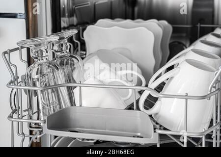 Im Korb des Geschirrspülers befindet sich eine Menge sauberes Geschirr. Tassen und Teller glänzen nach dem Waschen, Nahaufnahme Stockfoto
