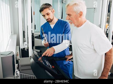 Leitender Patient, der mit seinem Therapeuten im Krankenhaus eine Physiotherapie durchgeführt hat. Ältere Mann Training auf dem Laufband. Stockfoto