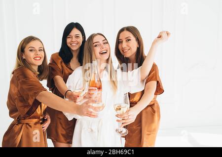 Schlafanzug Party time. Schöne charmante Freundinnen feiern Junggesellinnenabschied, trinken Alkohol und lachen im Hotel Stockfoto