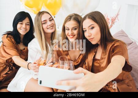 Freundinnen tragen Satin Roben feiern Henne Party. Frauen, die Alkohol trinken und zusammen Selfie machen Stockfoto