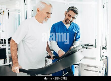 Leitender Patient, der mit seinem Therapeuten im Krankenhaus eine Physiotherapie durchgeführt hat. Ältere Mann Training auf dem Laufband. Stockfoto