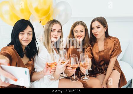 Freundinnen tragen Satin Roben feiern Henne Party. Frauen, die Alkohol trinken und zusammen Selfie machen Stockfoto
