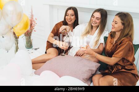 Schlafanzug Party time. Schöne charmante Freundinnen feiern Junggesellinnenabschied, trinken Alkohol und lachen im Hotel Stockfoto