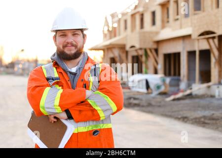 Vorarbeiter in orangefarbener Arbeitskleidung, der das Notizbuch auf der Baustelle hält. Stockfoto