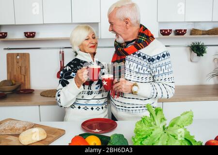 Ältere glückliche Paar trinken Latte zu Hause in der Küche stehen, Senioren Menschen verbringen Zeit zusammen zu Hause. Stockfoto