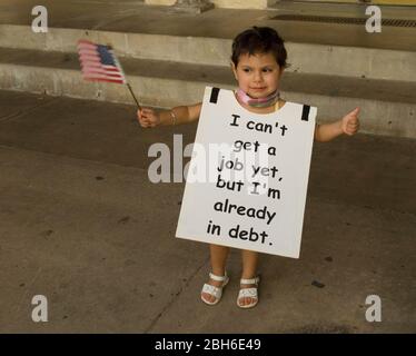 San Antonio, Texas 15. April 2009:das Kind trägt ein Protestschild mit der Aufschrift: „Ich kann noch keinen Job bekommen, aber ich bin bereits verschuldet“ und hält während einer „Tea Party“-Kundgebung eine kleine amerikanische Flagge vor der Alamo, die gegen die Rettungsaktionen des Bundes und die Wirtschafts- und Einwanderungspolitik von Präsident Obama protestiert. ©Bob Daemmrich Stockfoto